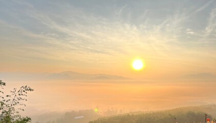 A serene sunrise casts a golden glow over misty mountains and valleys, creating a peaceful, tranquil landscape.