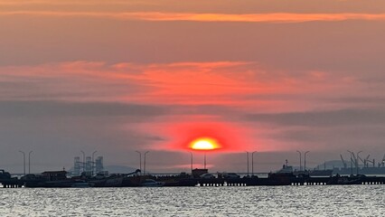Obraz premium A serene sunset over a harbor, with silhouettes of boats and wind turbines, casting a warm glow on the water.
