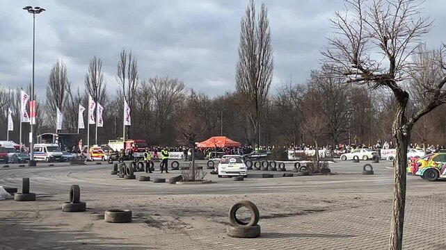 A lively car event in an open parking area in Krakow, Poland, featuring drift cars, spectators, flags, and safety barriers. The scene captures the thrill and energy of a motorsport gathering.