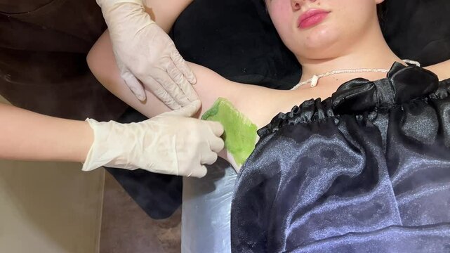 The hands of the beautician woman are applying sugar paste to the girl's skin.
