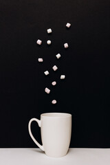 White mug with colorful marshmallows falling against a black background, creating a playful and inviting hot beverage concept