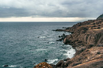 Coastal view with rocky shoreline and cloudy sky at the ocean's edge during late afternoon