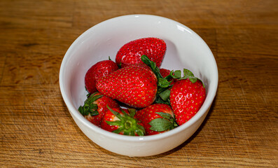 Strawberries in a deep plate on a kitchen cutting board.
