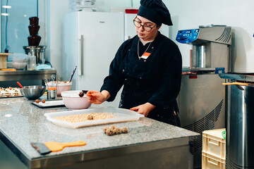 Pastry chef dipping praline in melted chocolate in professional kitchen