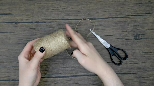Women's hands unwind a string from a spool and cut a piece with scissors. Diy craft concept.