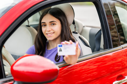 Young woman showing driving license while sitting in a red car - Powered by Adobe