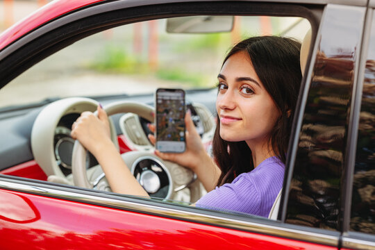 Young woman driving car and using navigation app on smartphone