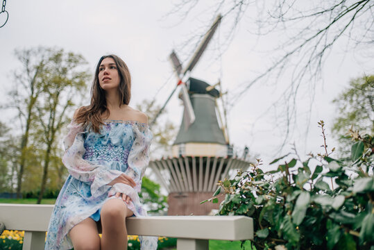 Happy woman tourist posing near a traditional windmill in a flower park.
