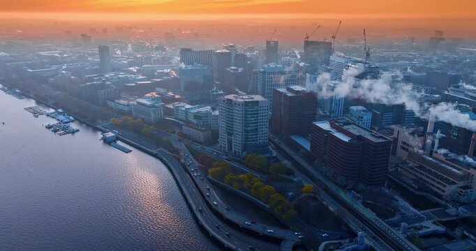 Scenic view of Boston coated in fog and orange light of setting sun. Drone footage above the waterscape of the Charles River.