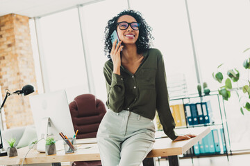 Young businesswoman talking on the phone while smiling at her desk in a bright modern office