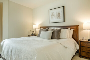A minimalist bedroom with a wooden headboard, neutral bedding, and framed artwork, offering a clean and serene space for relaxation and comfort