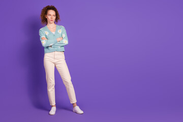 Young woman with crossed arms in stylish cardigan standing against purple background, expressing...