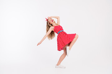 Dynamic young woman in a stylish retro red polka dot dress performs an energetic dance against a...