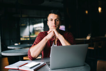 Thoughtful man sitting at table with laptop in cafe