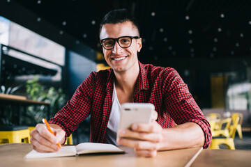 Cheerful freelancer with smartphone making notes