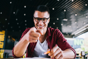 Cheerful young man pointing at camera in cafe