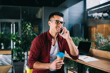 Smiling man with takeaway beverage talking on smartphone
