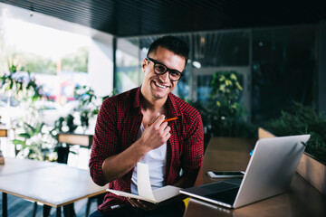 Cheerful man with notepad and pen in hands in cafe
