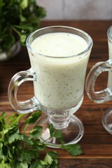 Healthy parsley drink in glass and leaves on wooden table, closeup