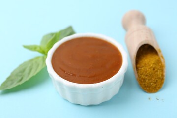 Tasty curry sauce, powder and basil leaves on light blue background, closeup