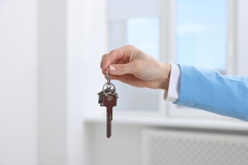 Real estate agent holding key with house shaped keychain indoors, closeup
