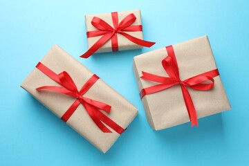 Many gifts wrapped in kraft paper with bow on light blue background, flat lay