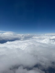 Fluffy white clouds stretch endlessly under a deep blue sky, capturing a peaceful scene from above the atmosphere during flight.