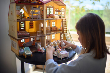 Little girl playing alone with a toy house and small animal figures in a cozy kids’ room. Imaginative playtime, quiet moment of childhood, indoor activity.