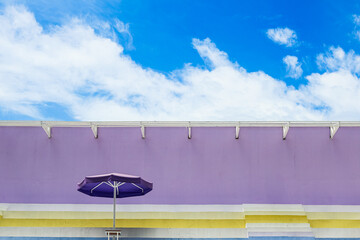 Colorful stadium seats with umbrellas under blue sky and purple wall on sunny day.