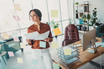 Confident young female professional in modern office setting with sticky notes and creative...