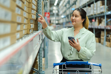 female warehouse manager checks inventory while holding smartphone and managing shipping orders in...