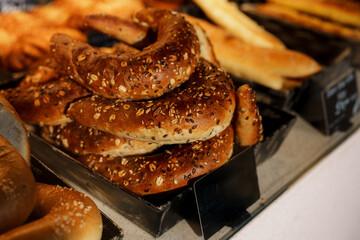 Warm, inviting whole grain rolls topped with sesame seeds are neatly stacked in a bakery display case, alongside other tempting bread products, creating a visual feast for pastry lovers