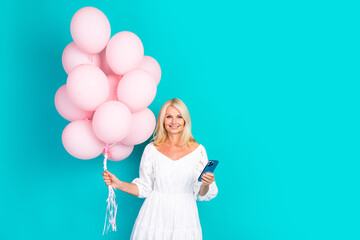 Smiling blonde woman holding pink balloons and smartphone against a turquoise background