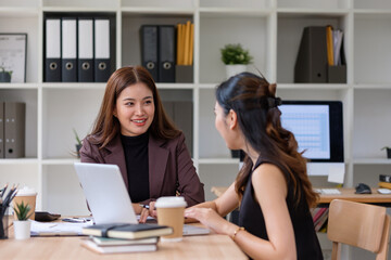 Businesswomen reviewing documents and working on laptops in modern office.