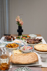 Table is set for a festive meal, featuring a variety of traditional dishes, salads, roasted meat, pies, and a vase of flowers