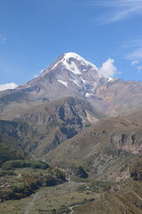 Fototapeta premium Mount Kazbek, a majestic snow-capped peak in Kazbegi, Georgia, towers above the Caucasus mountain landscape. A stunning scene perfect for travel, adventure, nature, and cultural destination themes.