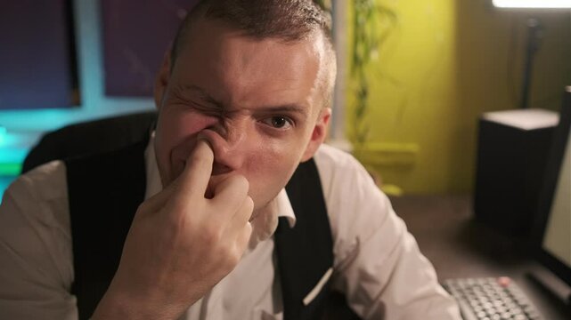 An office worker, dressed in formal attire, is seen picking his nose during work hours at his desk, suggesting a lapse in professional etiquette.