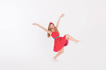 Blonde young woman in a retro polka dot dress leaping joyfully on a white background