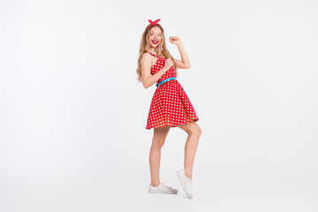 Young woman in retro polka dot dress striking a cheerful pose with vibrant energy against a white...
