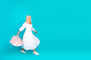 Mature stylish woman in a white summer dress walking and carrying shopping bags against a vibrant...
