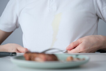 Spilled tough grease stain on clothes. Unrecognizable person siting at a dining table preparing to...