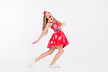 Young woman in retro red polka dot dress dancing with a cheerful expression against a white...