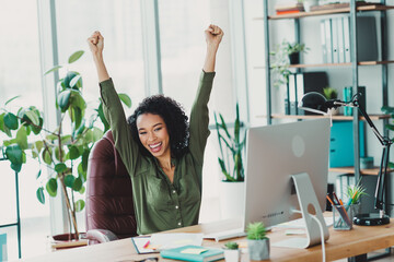 Successful businesswoman celebrating achievement at office desk in modern workplace with natural...