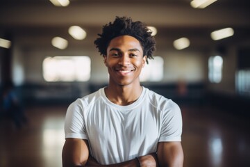 Fototapeta premium Smiling portrait of a teenage male African American basketball player wearing a white t shirt in an indoor basketball gym