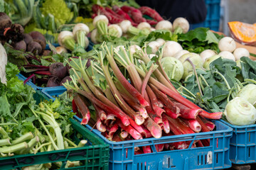 A blue crate of red radishes sits on a table next to a crate of green vegetables