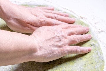 Fototapeta premium Women's hands roll out green dough with spinach with a rolling pin. The concept of healthy eating. Top view.