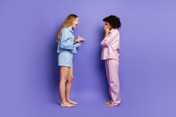 Two young female friends in pajamas showing contrasting emotions while standing against a vibrant purple backdrop