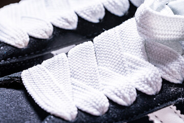 Lace-up on sneakers close-up. White, wide laces in black sneakers.