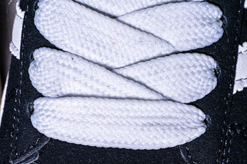 Lace-up on sneakers close-up. White, wide laces in black sneakers.