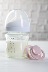 Feeding bottle with milk and pacifier on white wooden table